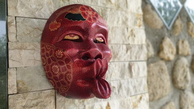 Red traditional Batak mask hanging on stone wall