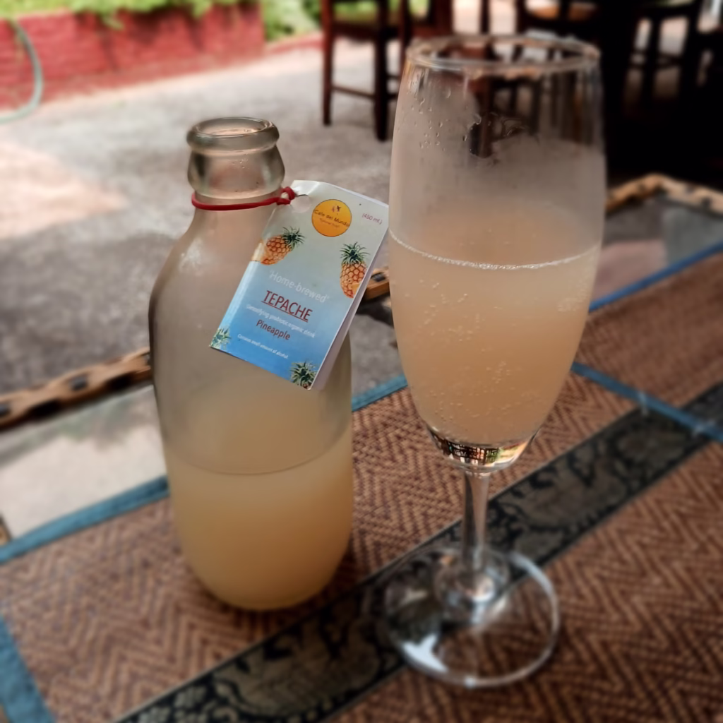 A small bottle of pineapple Tepache and a champagne flute. Both half full